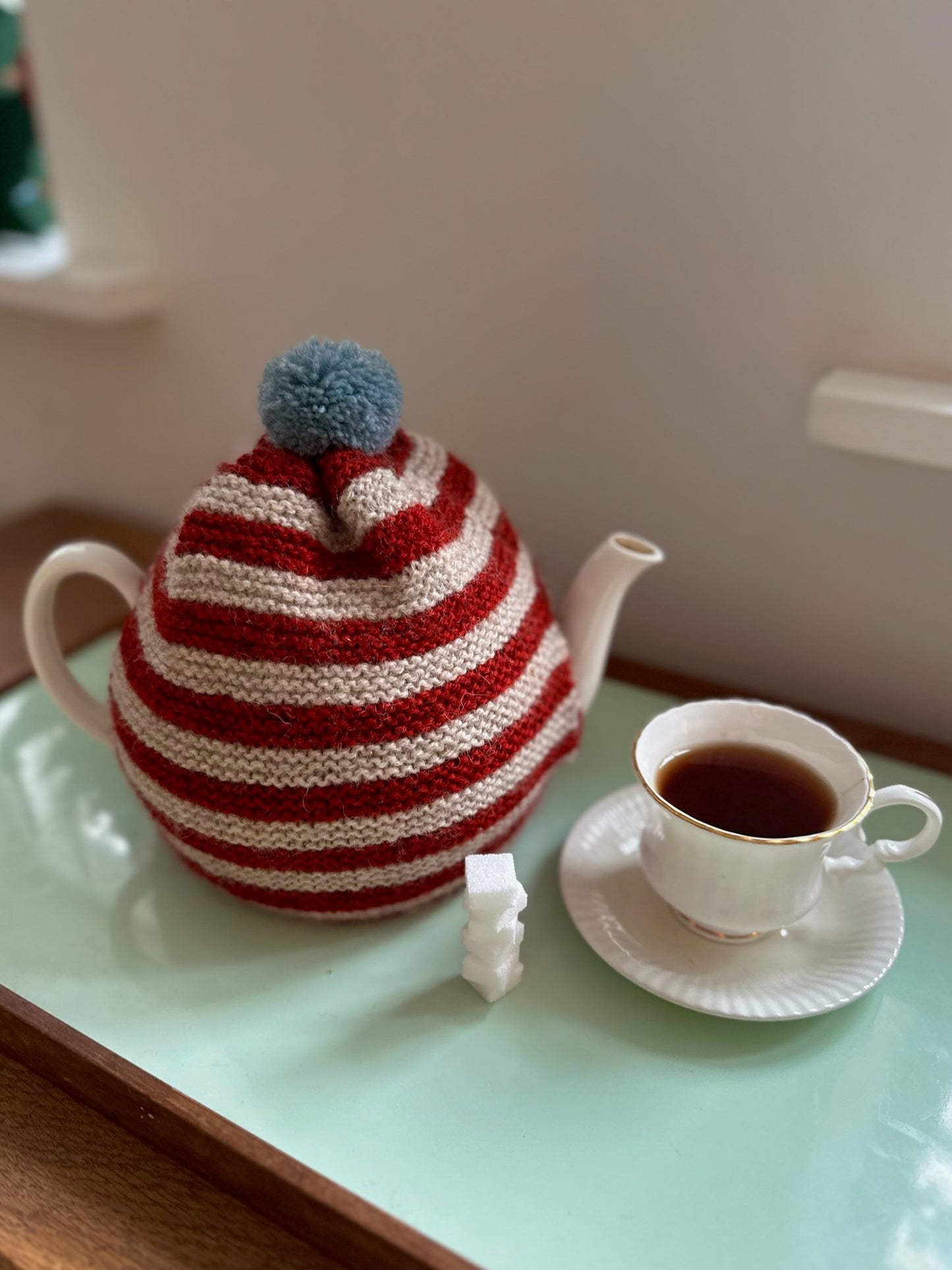 Håndstrikket tehætte med pompon - rød og beige stribet